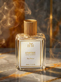 Perfume bottle labeled '1+1 Empire' with gold cap on a reflective surface with smoke effect.